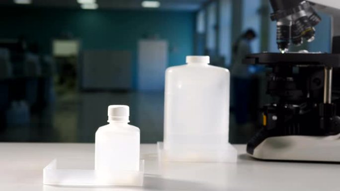 现代实验室概念。科学家在黑色手套把白色塑料瓶容器与显微镜背景。复制注释空间。4 k镜头