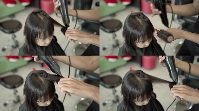 美发师在美容院用吹风机吹干小女孩的头发。美发沙龙的亚洲小女孩。小女孩拥有幸福，享受护发。手持镜头，真