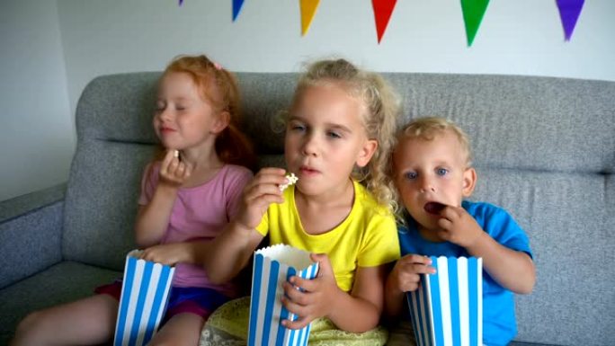 孩子们吃爆米花和看电影。坐在沙发上的小孩