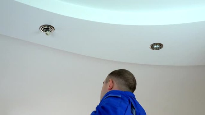 年轻电工将卤素聚光灯安装或更换到天花板