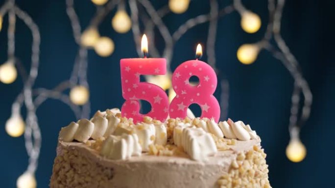 蓝色背景上有58号粉色蜡烛的生日蛋糕。蜡烛吹灭了。慢动作和特写视图