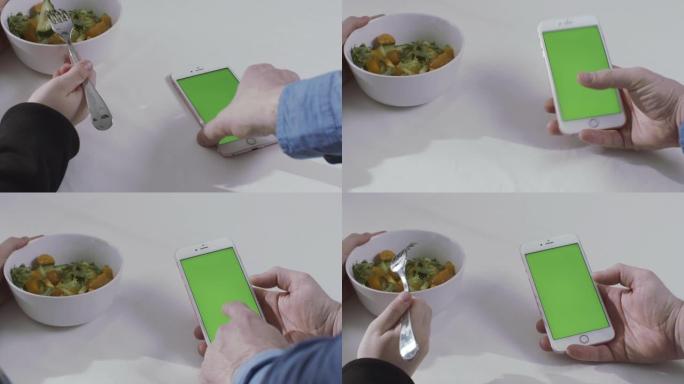 桌子上男人和女人的手的特写。库存镜头。男人使用带有色度键绿色屏幕的智能手机，女人拿着叉子吃蔬菜