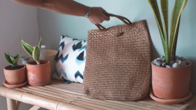 客厅天然竹椅上的女人手抓柳条购物袋，有机生活方式