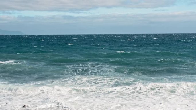 海上冲浪。海洋海岸，碧绿的海水和白色泡沫上的波浪。水滴飞入相机，火山黑岸的石头和沙子