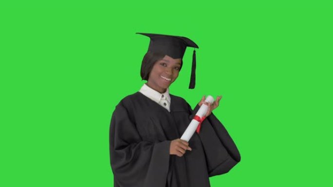 美丽的学生戴着毕业帽和礼服在绿色屏幕上微笑，色度键