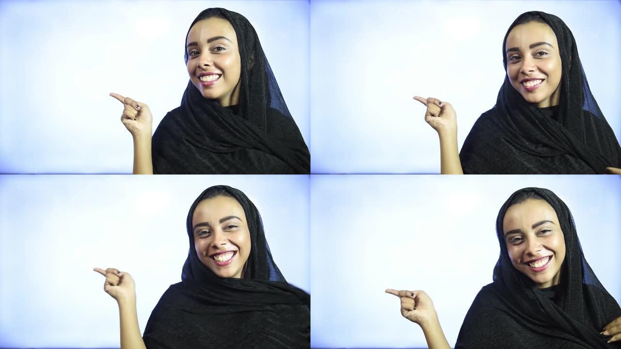 站立的穆斯林女孩戴着头巾，表现出举起手并微笑的东西