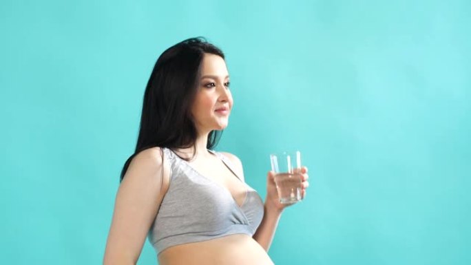 年轻的怀孕白种人模型，长长的黑发从玻璃杯中喝最纯净的水