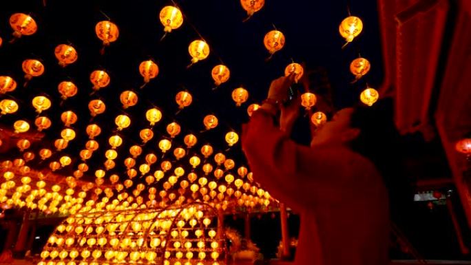 女人在神社为许多中国灯笼拍照。灯笼上的祝福文字含义有财富和幸福