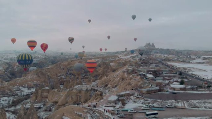 卡帕多西亚日出时，五颜六色的热气球在白雪皑皑的童话烟囱上