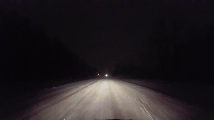夜间在乡村道路上迎面驶来的车灯在暴风雪中行驶。司机的观点POV在冬天晚上朝着明亮的前灯下雪。