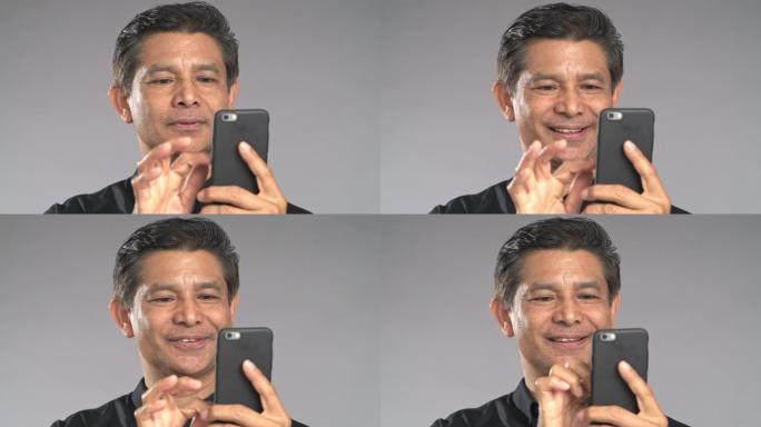 特写高级男子使用手机浏览，非常开心的微笑，孤立在灰色背景中。穿着黑色衬衫的亚洲男人。