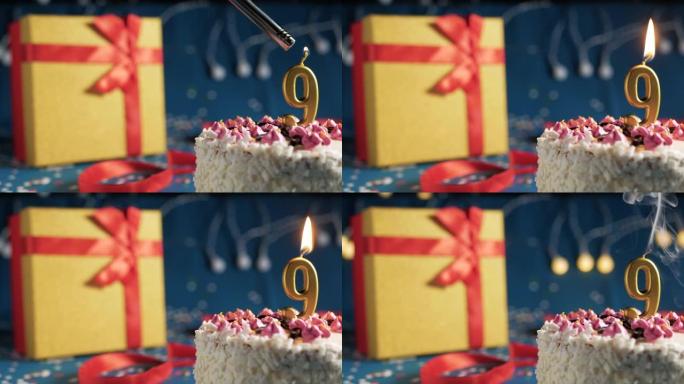 白色生日蛋糕9号点火器燃烧的金色蜡烛，蓝色背景带灯和用红丝带捆绑的礼物黄色盒子。特写