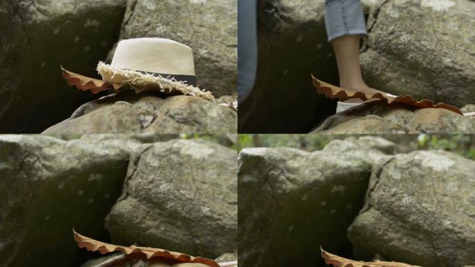 女人拿起草帽，在热带丛林中走过岩石。