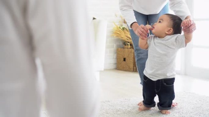 亚洲男婴幼儿迈出第一步。父亲和母亲的家人鼓励儿子学习在家走路