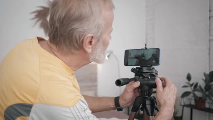现代祖父，一位老年男性博客作者在智能手机上设置了一个摄像头，以在他的房间内为vlog创建视频内容