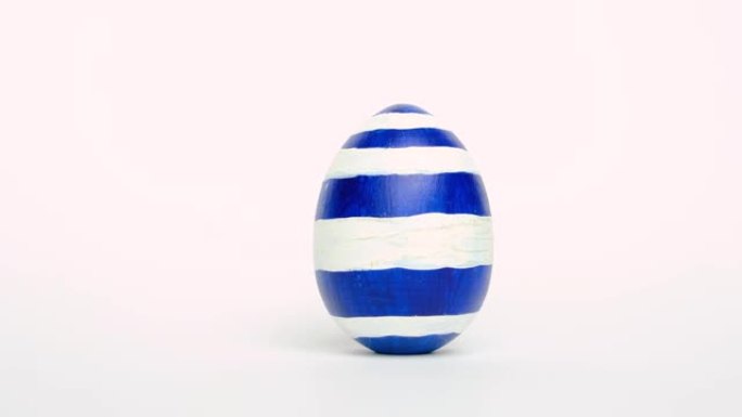 复活节彩蛋在滚动，互相敲在白色的桌子上。鸡蛋时尚彩色经典蓝色、白色和金色。复活节快乐。最小风格