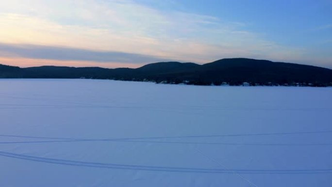 加拿大魁北克日落时雪上有雪地摩托痕迹的湖泊的4k航拍视频视图