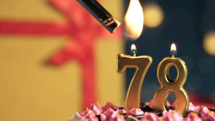 生日蛋糕编号78点灯燃烧的金色蜡烛，蓝色背景礼物黄色盒子用红丝带绑起来。特写和慢动作