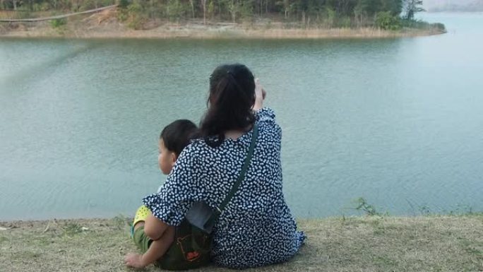 一位亚洲母亲带着孩子坐在河边