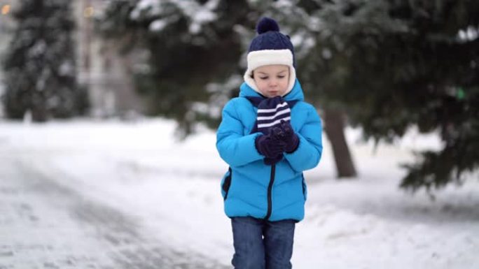 穿着蓝色冬布的可爱的四岁男孩在雪街散步。