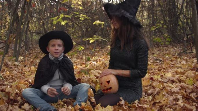 男孩和妈妈穿着万圣节服装在秋天的森林里玩耍。