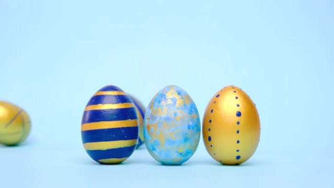 复活节彩蛋在滚动，互相敲在蓝色的桌子上。鸡蛋时尚彩色经典蓝色、白色和金色。复活节快乐。最小风格