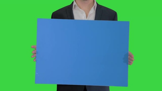 穿着西装的男人在绿色屏幕上拿着一块空白板，色键