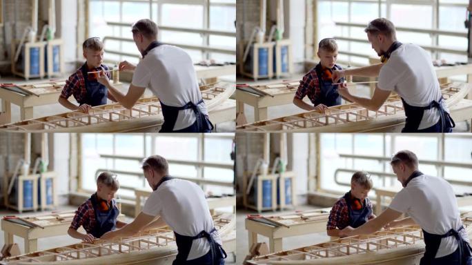中年木匠向好奇的小儿子展示如何在木工车间的工作台上建造木船