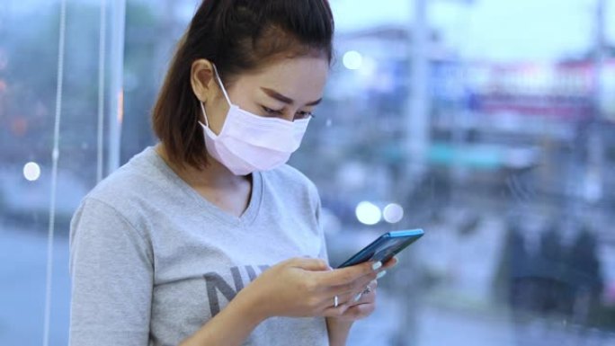 亚洲年轻女子在城市使用智能手机戴口罩，因为空气污染，微粒和保护流感病毒，流感，冠状病毒