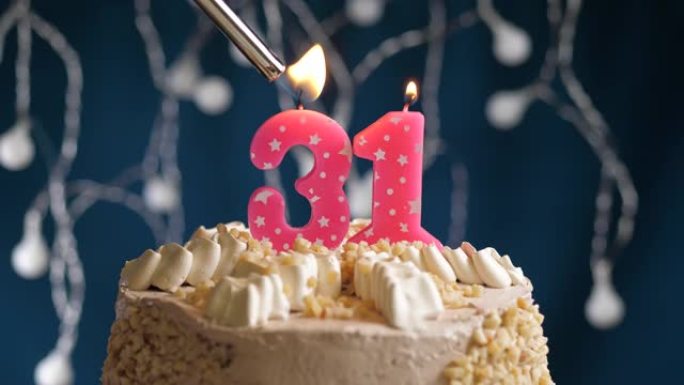 蓝色背景上有31号粉色蜡烛的生日蛋糕。蜡烛着火了。慢动作和特写视图