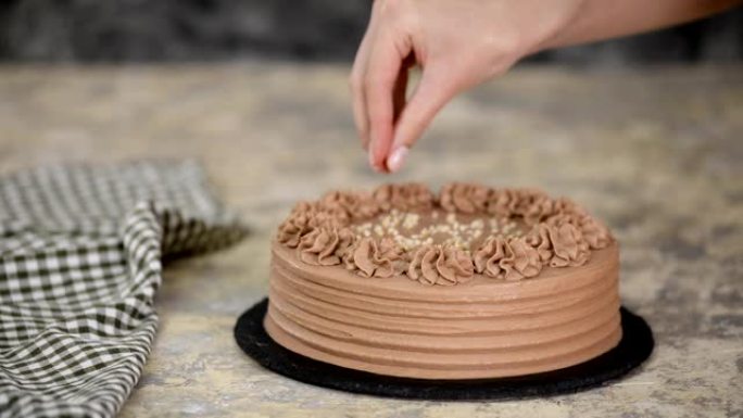 在巧克力海绵蛋糕的奶油上撒坚果的特写镜头。贝克用坚果装饰巧克力蛋糕。