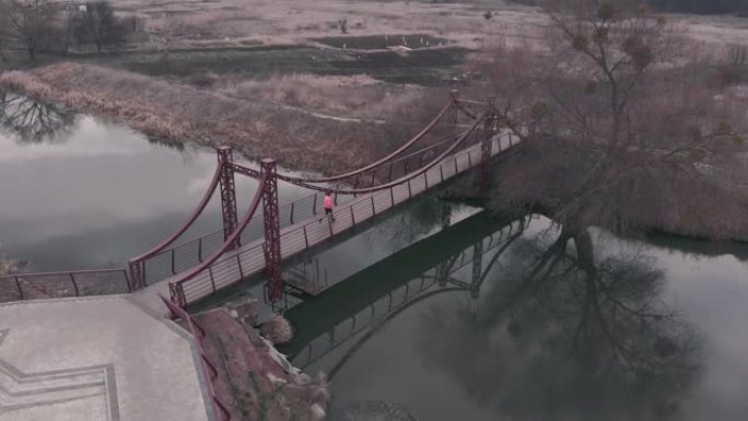 年轻的女孩在公园里奔跑，有河和桥。女运动员在人行天桥上跑步。休闲区女性慢跑