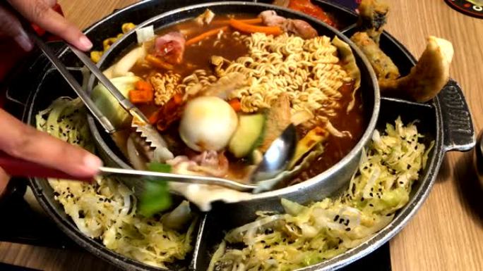 韩国火锅 “budae jjijae” 配黄色面条汤炖是韩国融合食品，融合了美式面条。用汤勺和钳子将