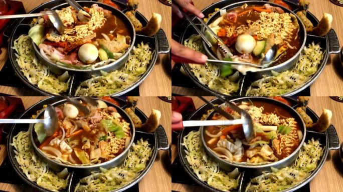 韩国火锅 “budae jjijae” 配黄色面条汤炖是韩国融合食品，融合了美式面条。用汤勺和钳子将
