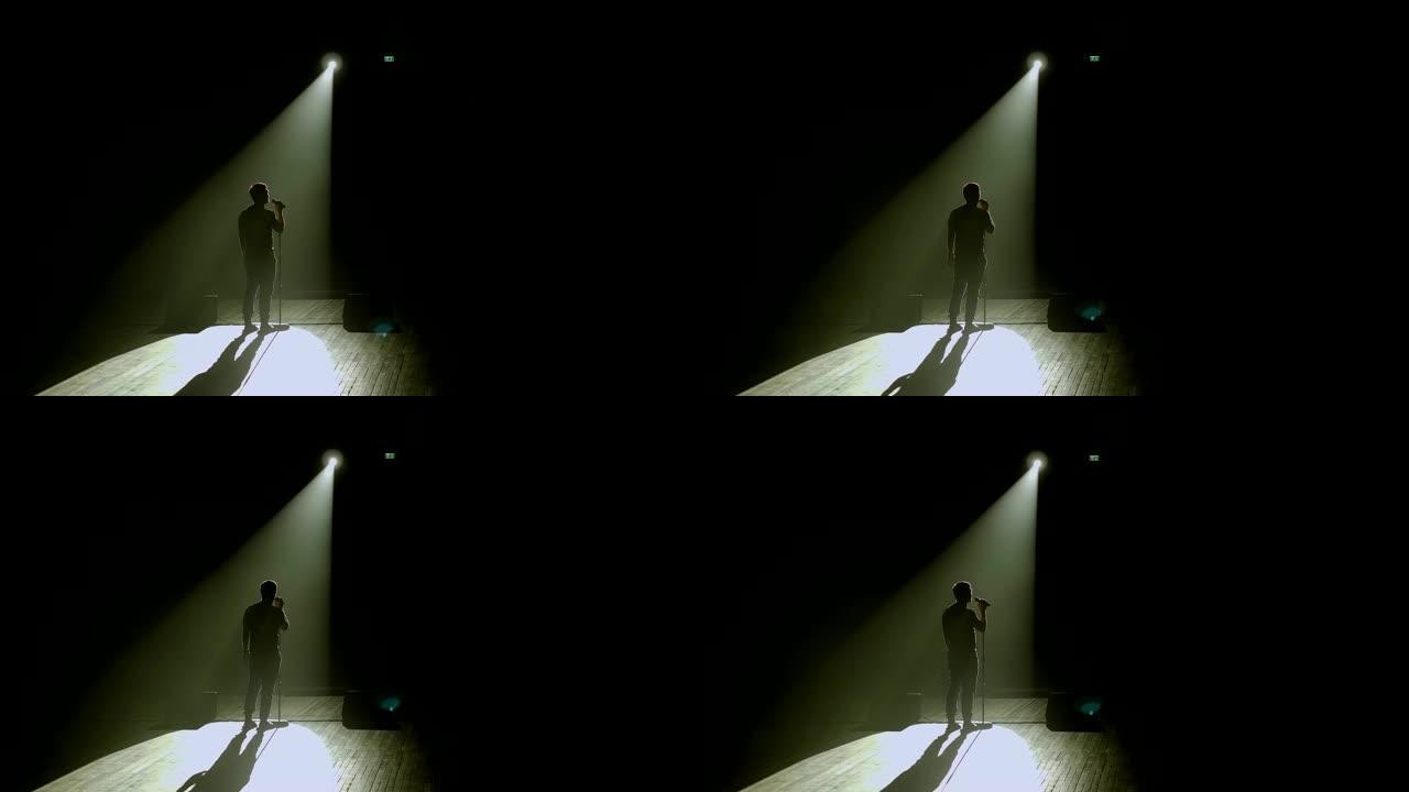 一个男人在黑暗中拿着麦克风在舞台上的剪影。演讲者。
