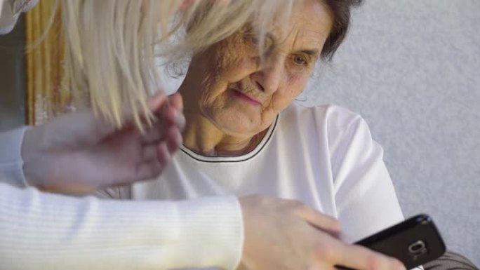 一位年轻女子向祖母展示了如何使用智能手机，她将其握在手中，并告诉一位老年妇女。