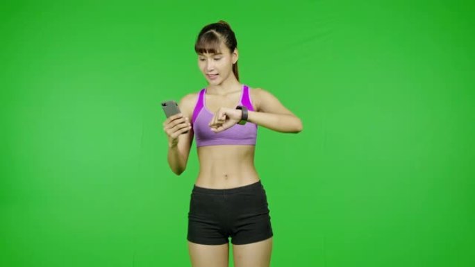 适合女性将智能手表与手机应用程序同步进行锻炼，绿屏，点头。穿着紫色布站在镜头前的亚洲运动女子。