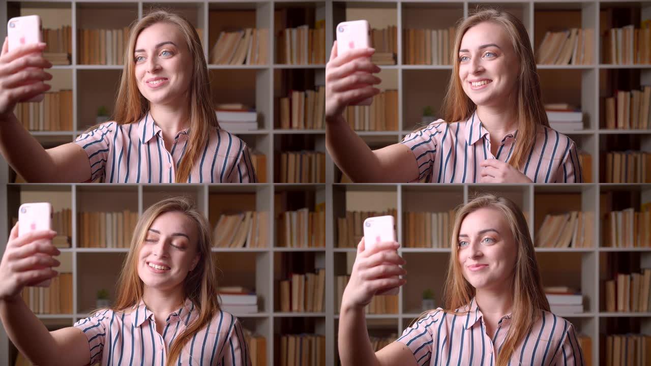 在大学图书馆里，年轻漂亮的白人女学生通过电话打视频的特写肖像