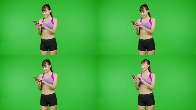 健康女性浏览手机，绿屏背景，健康身材，社交媒体交流。亚洲女运动员穿着紫色的衣服站在镜头前。