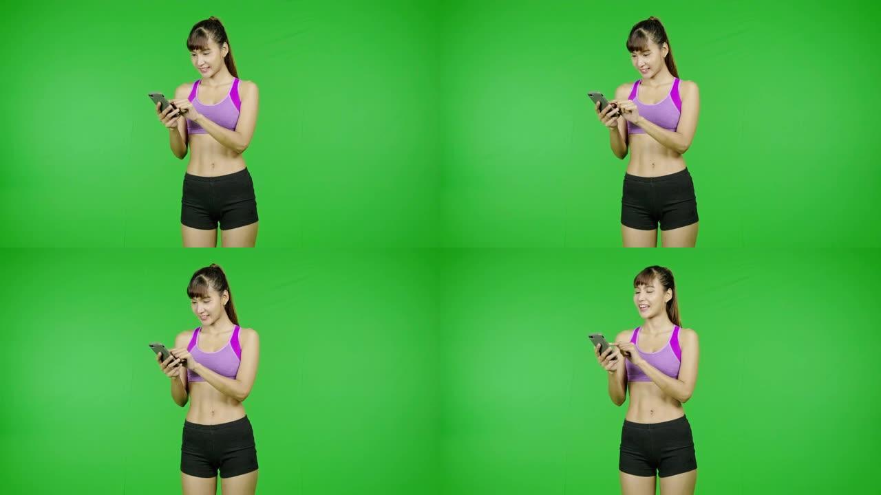 健康女性浏览手机，绿屏背景，健康身材，社交媒体交流。亚洲女运动员穿着紫色的衣服站在镜头前。