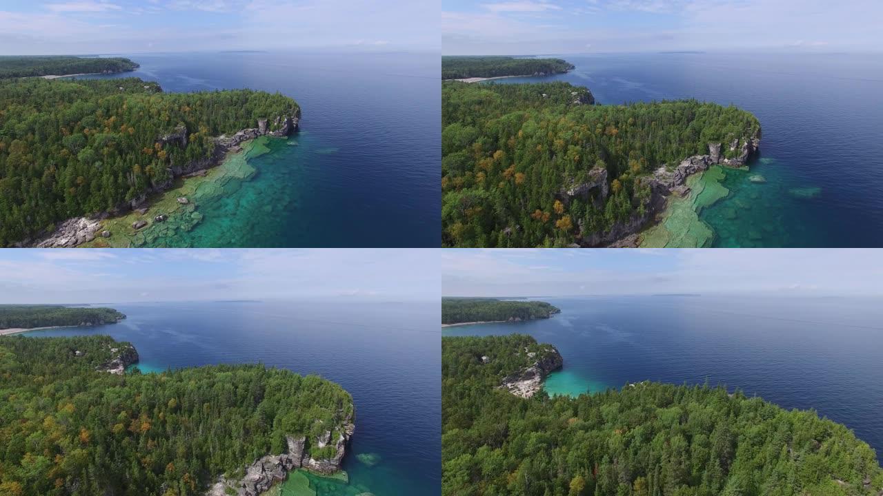 无人机在半岛上空缓慢飞行，松树林和碧蓝的海水