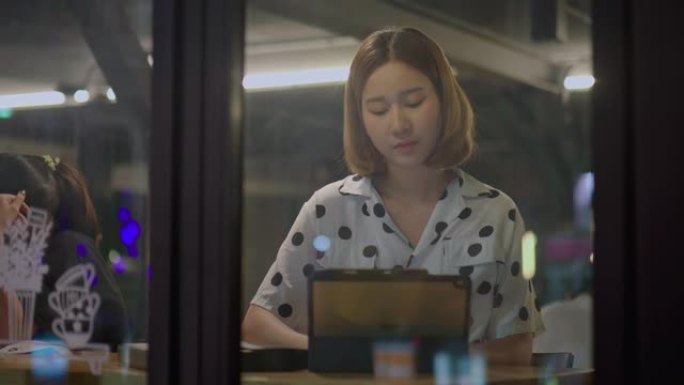 年轻的亚洲妇女晚上在醒来的太空咖啡店使用平板电脑