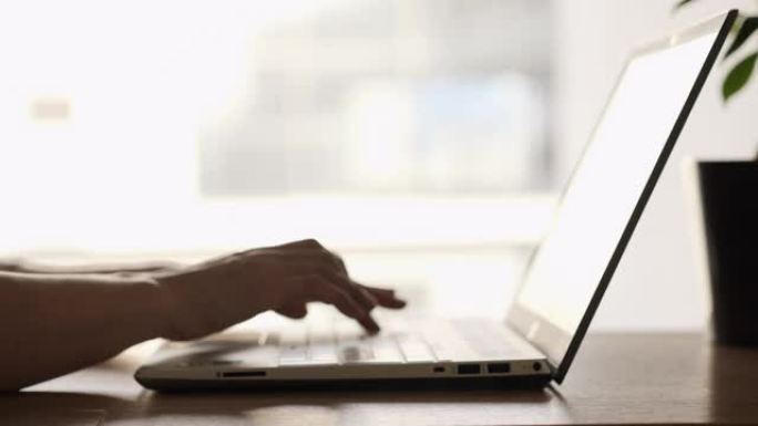 女人在窗户旁边的台式机上使用笔记本电脑。女性博客自由职业者在家庭办公室工作笔记本电脑。用键盘关闭女性