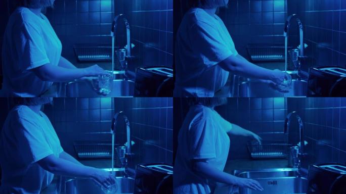 女人在现代厨房用霓虹灯打开水起重机，洗脏玻璃。