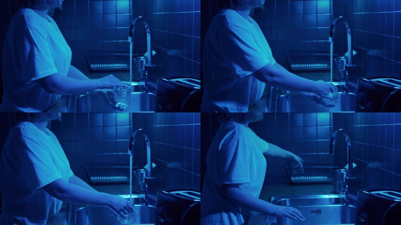 女人在现代厨房用霓虹灯打开水起重机，洗脏玻璃。