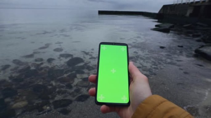 男性手持智能手机空白绿屏靠海