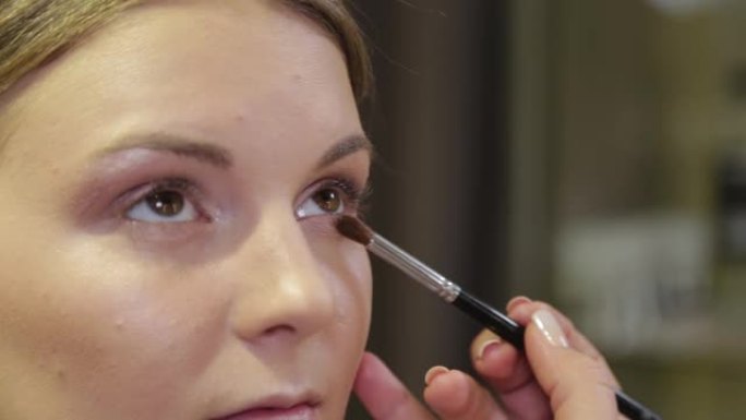 专业化妆师用刷子给美容院的客户涂眼影