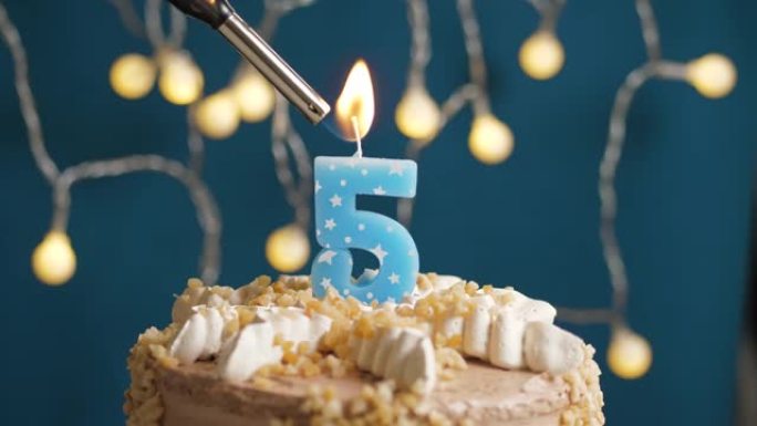 蓝色背景上有5个数字蜡烛的生日蛋糕。蜡烛着火了。慢动作和特写视图