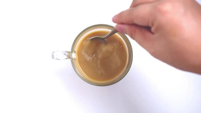 俯视图，人用手在白色背景上用勺子搅拌热牛奶咖啡或热牛奶茶