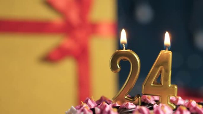 生日蛋糕编号24点灯燃烧的金色蜡烛，蓝色背景礼物黄色盒子用红丝带绑起来。特写和慢动作